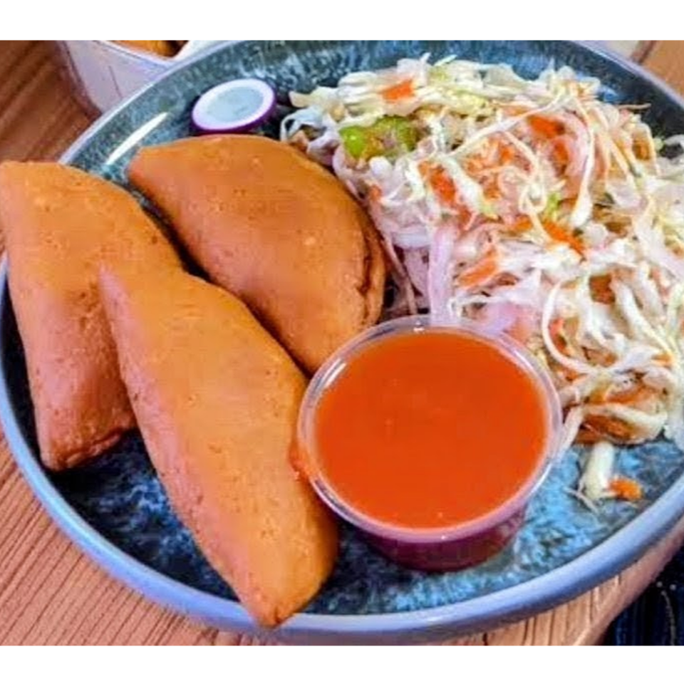 Plate of three golden fried pastries with shredded cabbage salad, dipping sauce, and sliced radish.