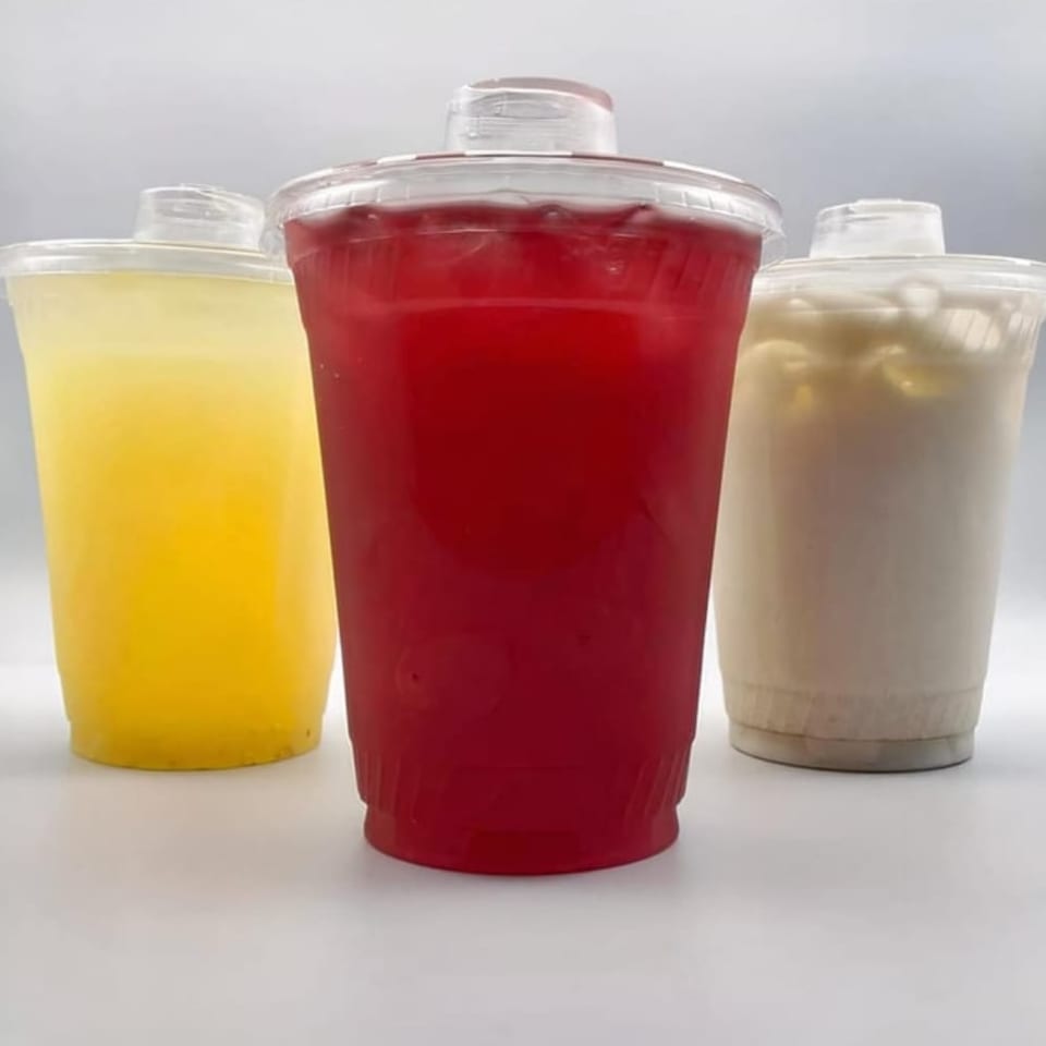 Three lidded plastic cups of yellow, red, and creamy white beverages arranged against a plain background.