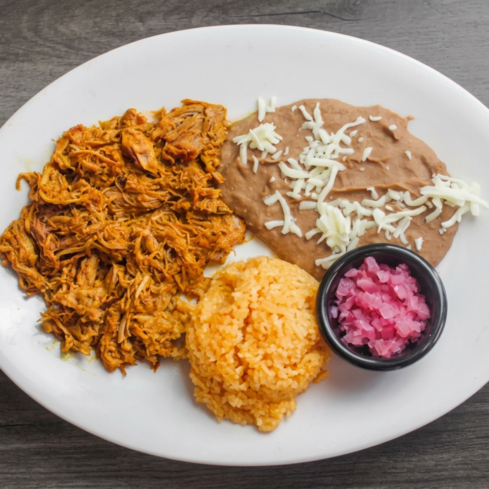 Plate of crispy shredded chicken, refried beans with cheese, Mexican rice, and pink pickled onions on a wooden table.