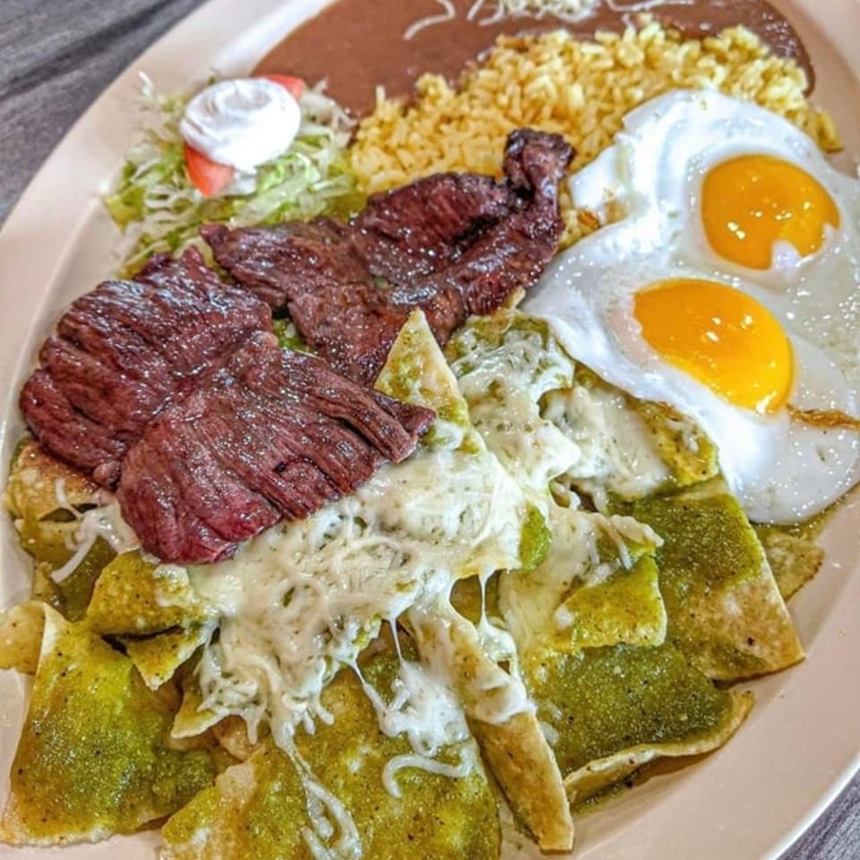 Mexican-style platter with grilled steak, two sunny-side-up eggs, rice, beans, salad, and cheesy green chilaquiles.