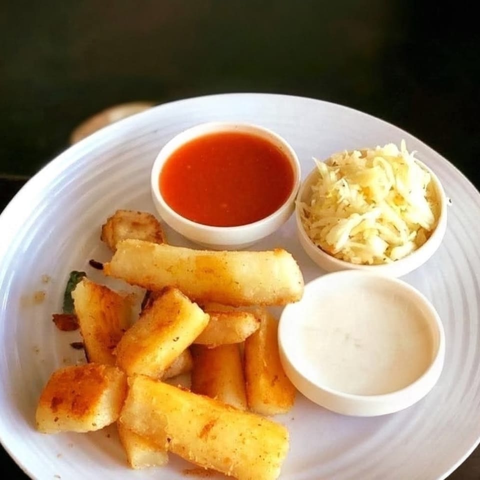 Plate of golden fried yuca sticks served with red dipping sauce, creamy white sauce, and shredded cabbage salad.