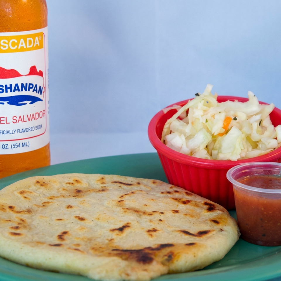 Salvadoran pupusa with curtido and salsa on a green plate beside a bottle of Kolashanpan soda.
